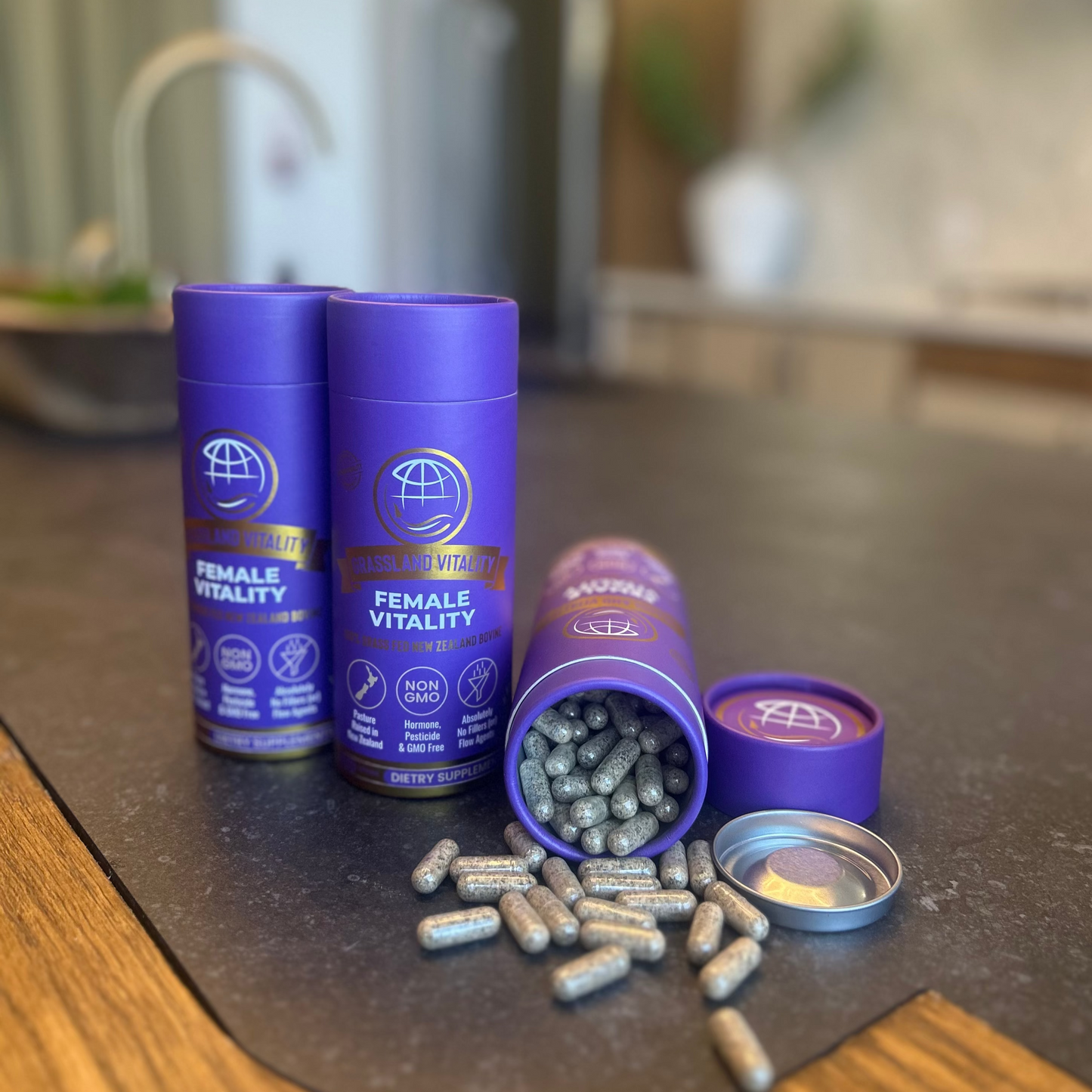 Two purple containers labeled 'Female Vitality' with their lids off, revealing capsules on a kitchen counter.